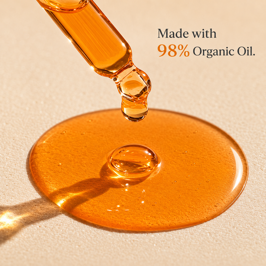 Close-up of organic oil being dripped onto a beige surface with text indicating 98% organic content.